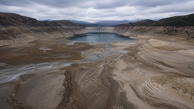 Un bacino artificiale con poca acqua, sedimenti emersi, fango secco e una diga isolata mostra il rischio nascosto della perdita di capacità dei serbatoi idrici.
